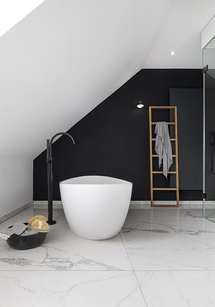 Badezimmer mit einer freistehenden, runden Badewanne vor einer schwarzen Wand und einem Handtuchhalter in Form einer Holzleiter.