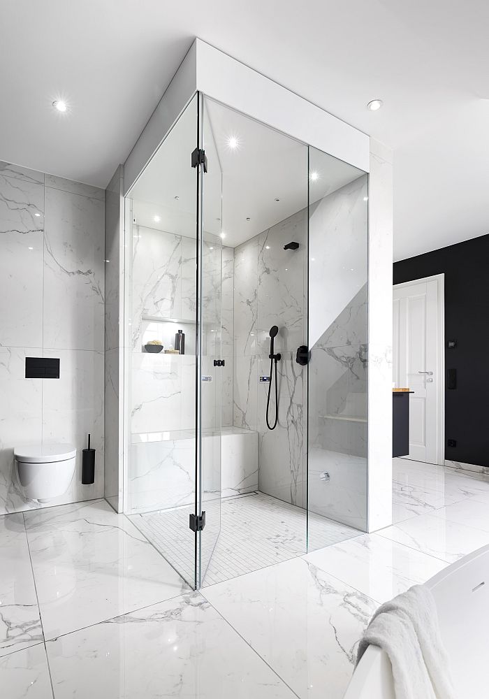 Badezimmer mit einer Glas-Dampfdusche, ausgestattet mit Marmorwänden und einer Sitzbank.