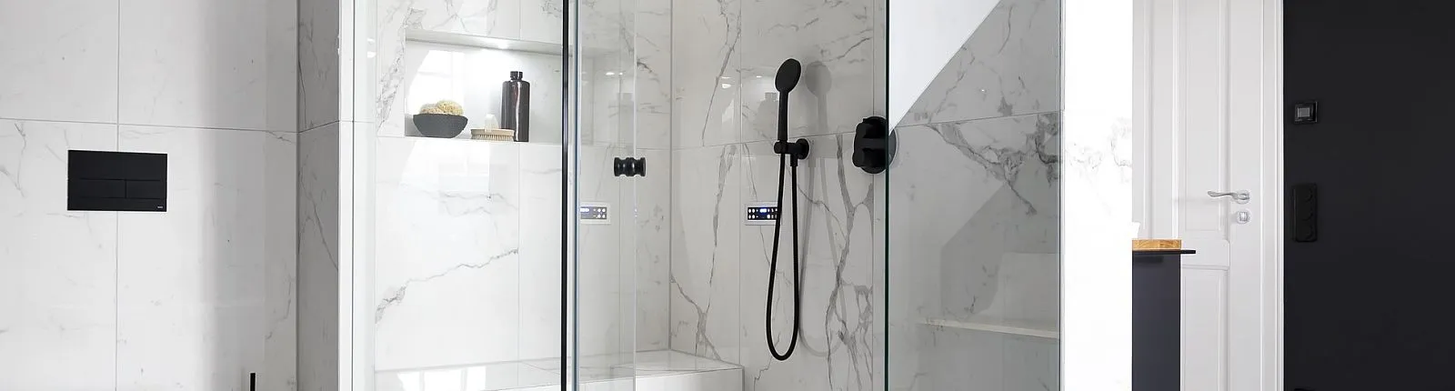 Geräumige Glasdusche mit weißen Marmorfliesen, die durch eine schwarze Handbrause und dunkle Bedienelemente ergänzt wird.