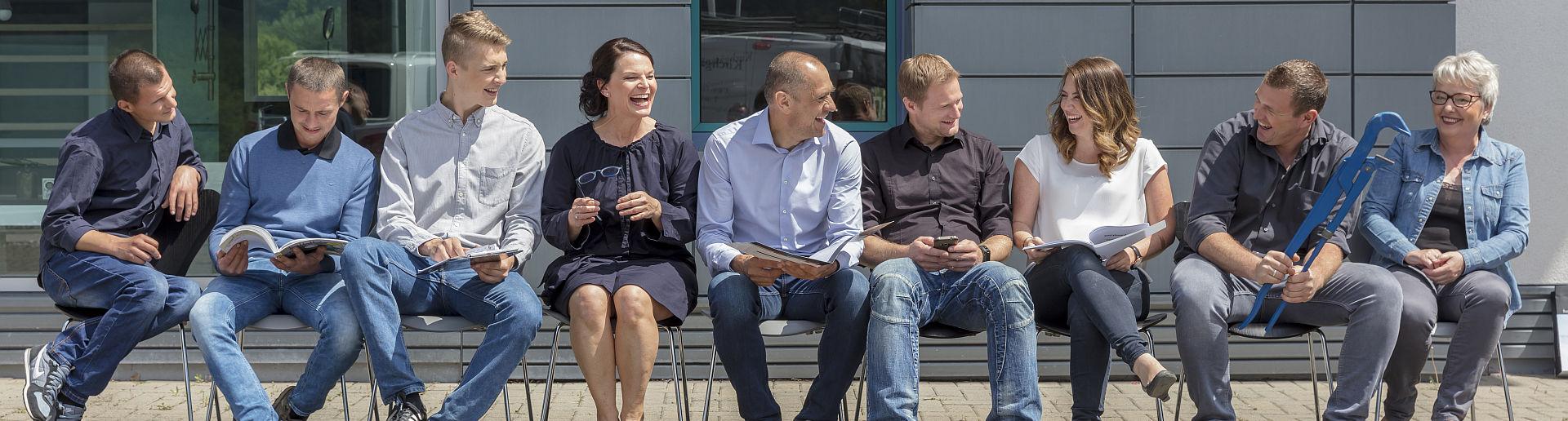 Das Team der Kirchgäßner GmbH sitzt lachend vor dem Firmengebäude.