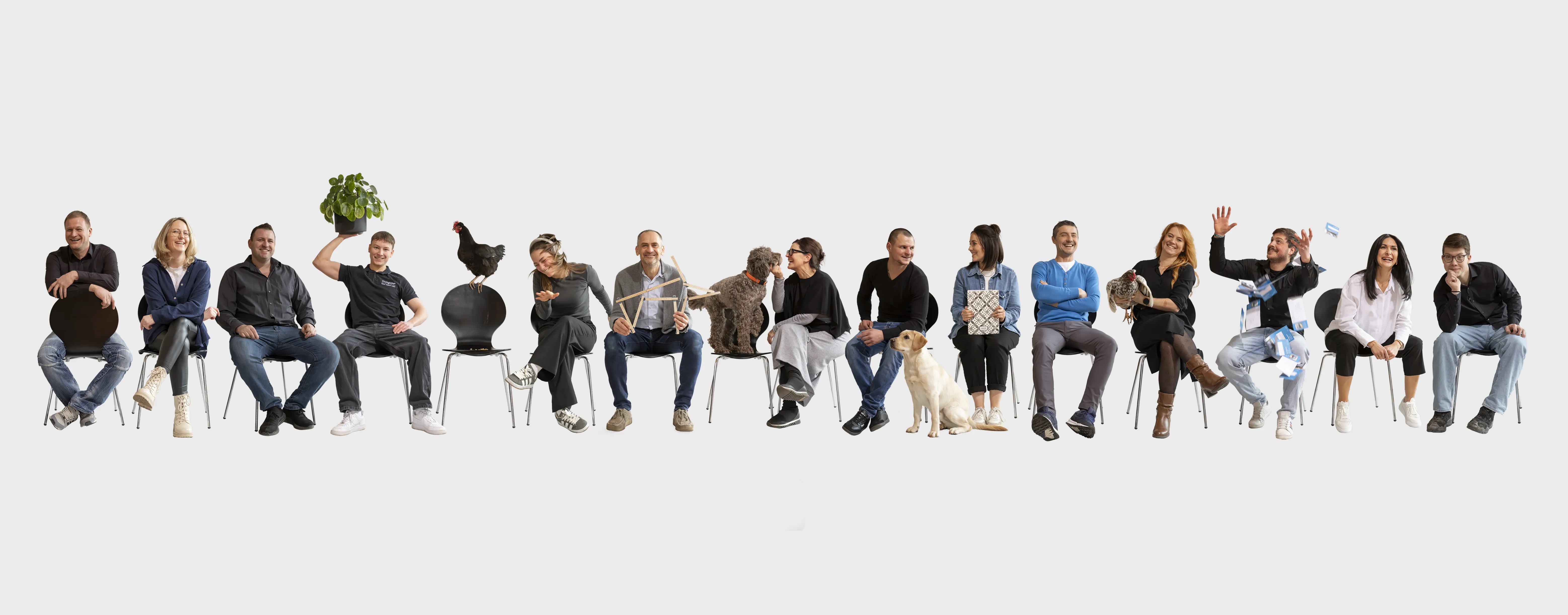 Gruppenbild des Teams Kirchgässner mit Mitarbeitenden und tierischen Begleitern in einer lockeren, humorvollen Inszenierung vor hellem Hintergrund.