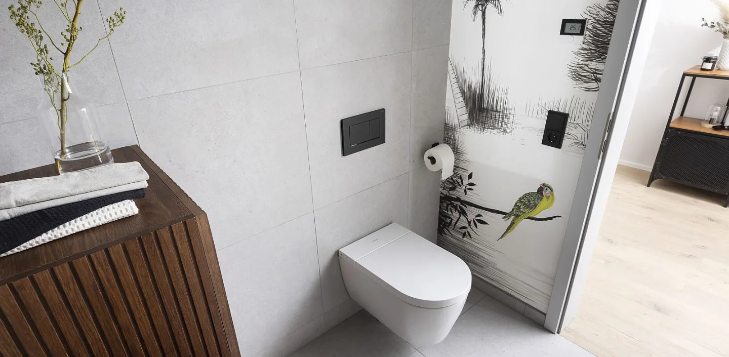 Gäste-WC mit weißer Toilette vor einer Wand mit detailreicher Naturtapete, die einen grünen Papagei und Palmen zeigt.