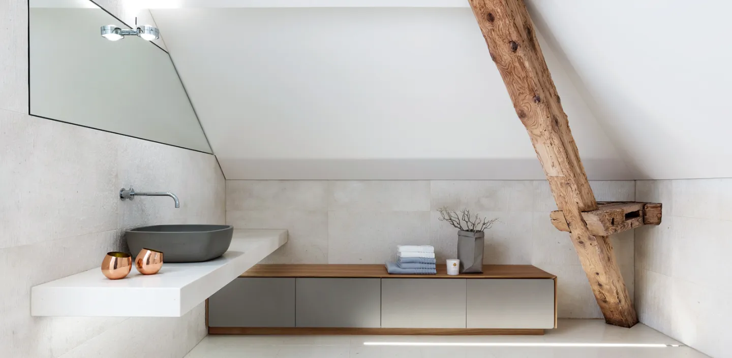 Dachbadezimmer mit schräger Decke, einem großen Wandspiegel und einer minimalistisch gestalteten Waschtischablage.