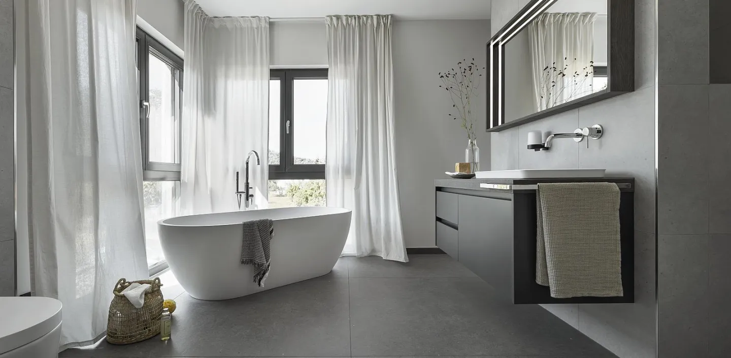 Helles Badezimmer mit Badewanne, großen Fenstern und minimalistischer Dekoration. Ein schlichter Waschtisch und ein Wandspiegel vervollständigen das Design.