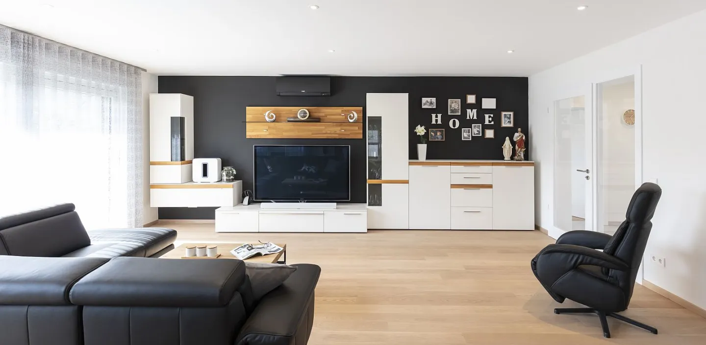 Geräumiges Wohnzimmer mit Holzboden und dunklen Sitzmöbeln.