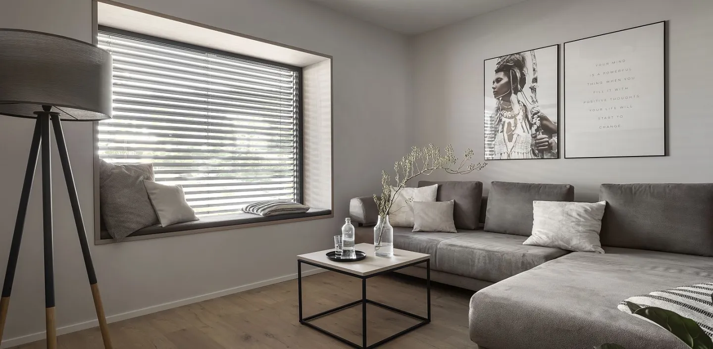 Wohnzimmer mit grauem Sofa, Couchtisch und großer Fensterbank mit Jalousie.