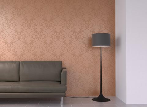 Eine orange Wand mit einer geschnörkelten Struktur dominiert den Hintergrund. Im Vordergrund befinden sich ein modernes Sofa und eine Stehlampe. Die Wandgestaltung verleiht dem Raum eine elegante und künstlerische Atmosphäre, während das Sofa und die Lampe eine gemütliche und einladende Stimmung schaffen.