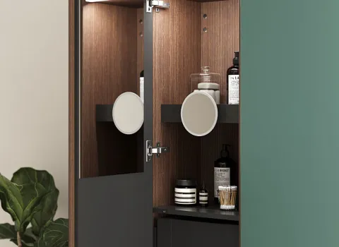 Der Badezimmerschrank Burgbad Lin20 ist geöffnet und zeigt ein stilvolles Holzfurnier mit dunklen Regalen, die verschiedene Pflegeprodukte und einen runden Kosmetikspiegel halten.