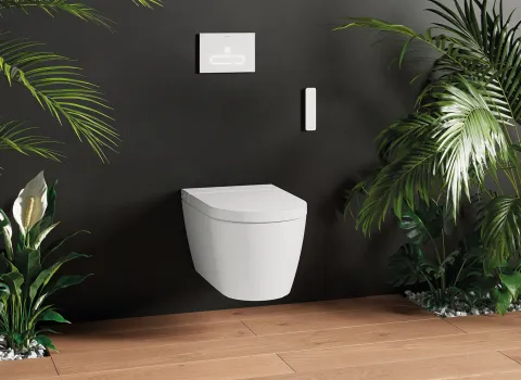 Weißes, wandhängendes Dusch-WC Starck f von Duravit vor dunkler Wand. Daneben stehen auf beiden Seiten große Pflanzen, die eine angenehme Atmospähre schafen.