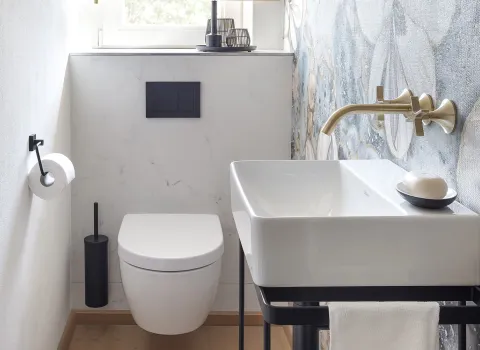 Helles Gäste-WC mit einer wandmontierten, weißen Toilette und einem rechteckigen Waschbecken mit goldener Armatur.