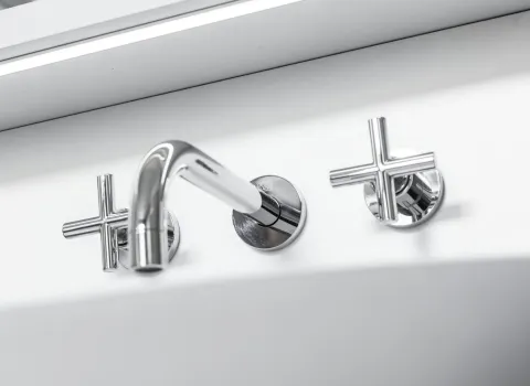 Chromfarbene Wandarmatur mit gebogenem Auslauf und zwei kreuzförmigen Griffen.