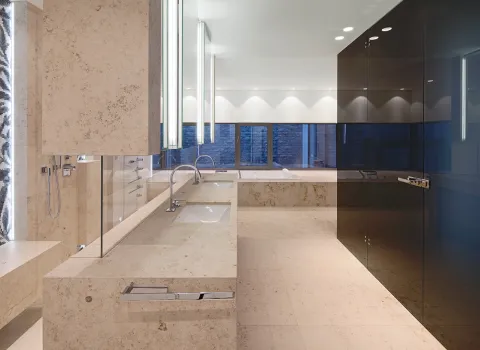  Badezimmer mit großflächiger Steinoptik und zwei integrierten Waschbecken, die von beleuchteten Spiegeln flankiert werden.