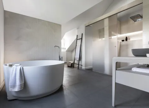 Freistehende Badewanne in einem Badezimmer mit Schiebetür zur Trennung von Dusche und WC.