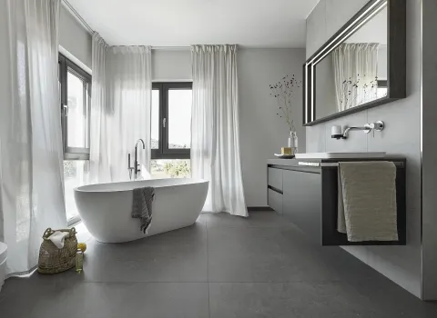 Helles Badezimmer mit Badewanne, großen Fenstern und minimalistischer Dekoration. Ein schlichter Waschtisch und ein Wandspiegel vervollständigen das Design.