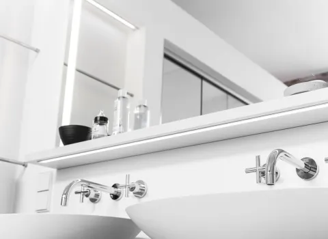 Zwei Wandarmaturen mit Kreuzgriffen über runden Waschbecken, die vor einem großen Spiegel installiert sind.