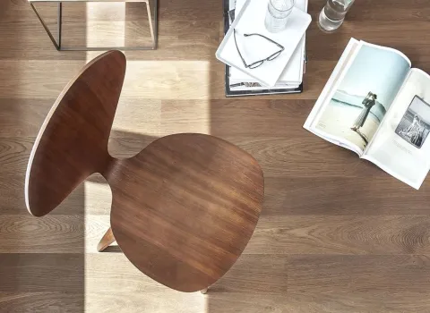 Ein dunkelbrauner Holzstuhl in einem hellen Raum, fotografiert von oben, steht auf einem warmen Holzboden. 