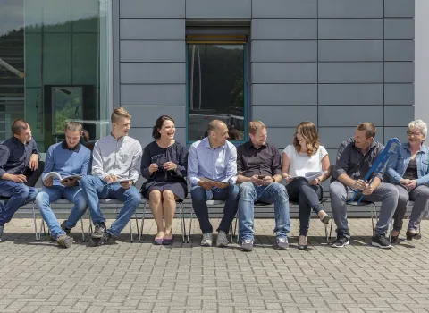 Das Team der Kirchgäßner GmbH sitzt lachend vor dem Firmengebäude.