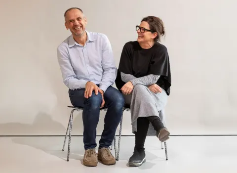 Hans und Anja Kirchgäßner, die Inhaber der Kirchgäßner bad & heizung GmbH in Freudenberg sitzen lachend auf Stühlen vor einer hellen Wand.