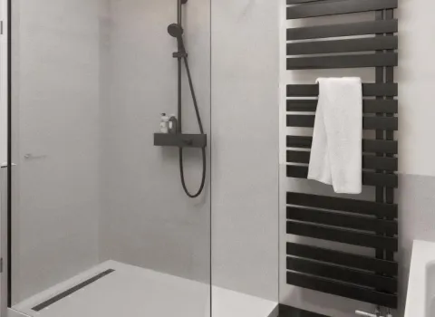 Dusche mit Glasabtrennung und Duschwanne. Armaturen, Badheizkörper und Bodenfliesen sind schwarz.