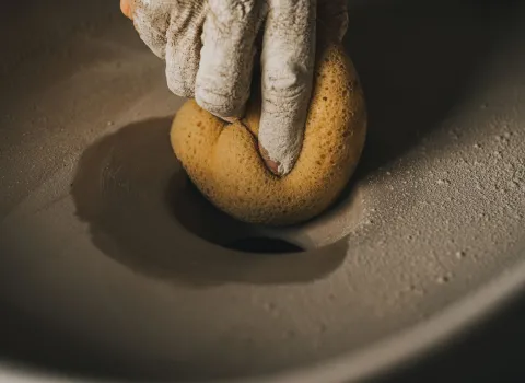Ein Handwerker mit staubiger Hand hält einen gelben Naturschwamm, mit dem er eine frisch gegossene Waschbecken-Oberfläche sorgfältig glättet.