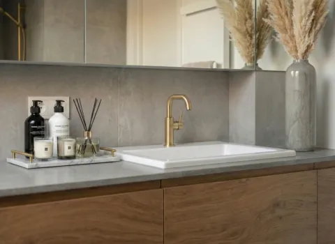 leganter Badezimmer-Waschtisch mit Holzfronten, Dekoration, Spiegel und goldener Designarmatur.