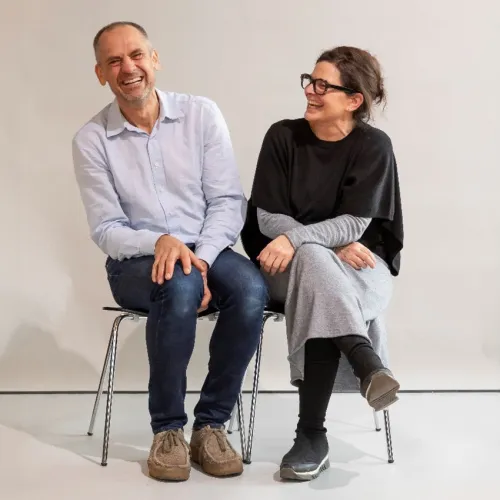 Hans und Anja Kirchgäßner, die Inhaber der Kirchgäßner bad & heizung GmbH in Freudenberg sitzen lachend auf Stühlen vor einer hellen Wand.