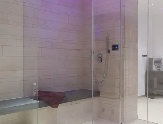 Ein modernes Dampfbad mit gläserner Abtrennung und Wänden aus großflächigen, beigen Fliesen in rechteckiger Form.