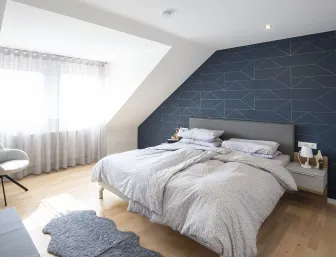 Helles Schlafzimmer mit einer stilvollen, dunklen Akzentwand hinter dem Doppelbett, die ein geometrisches Muster aufweist.