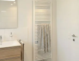 Weisser, wandhaengender Handtuchheizkörper in einem Badezimmer.