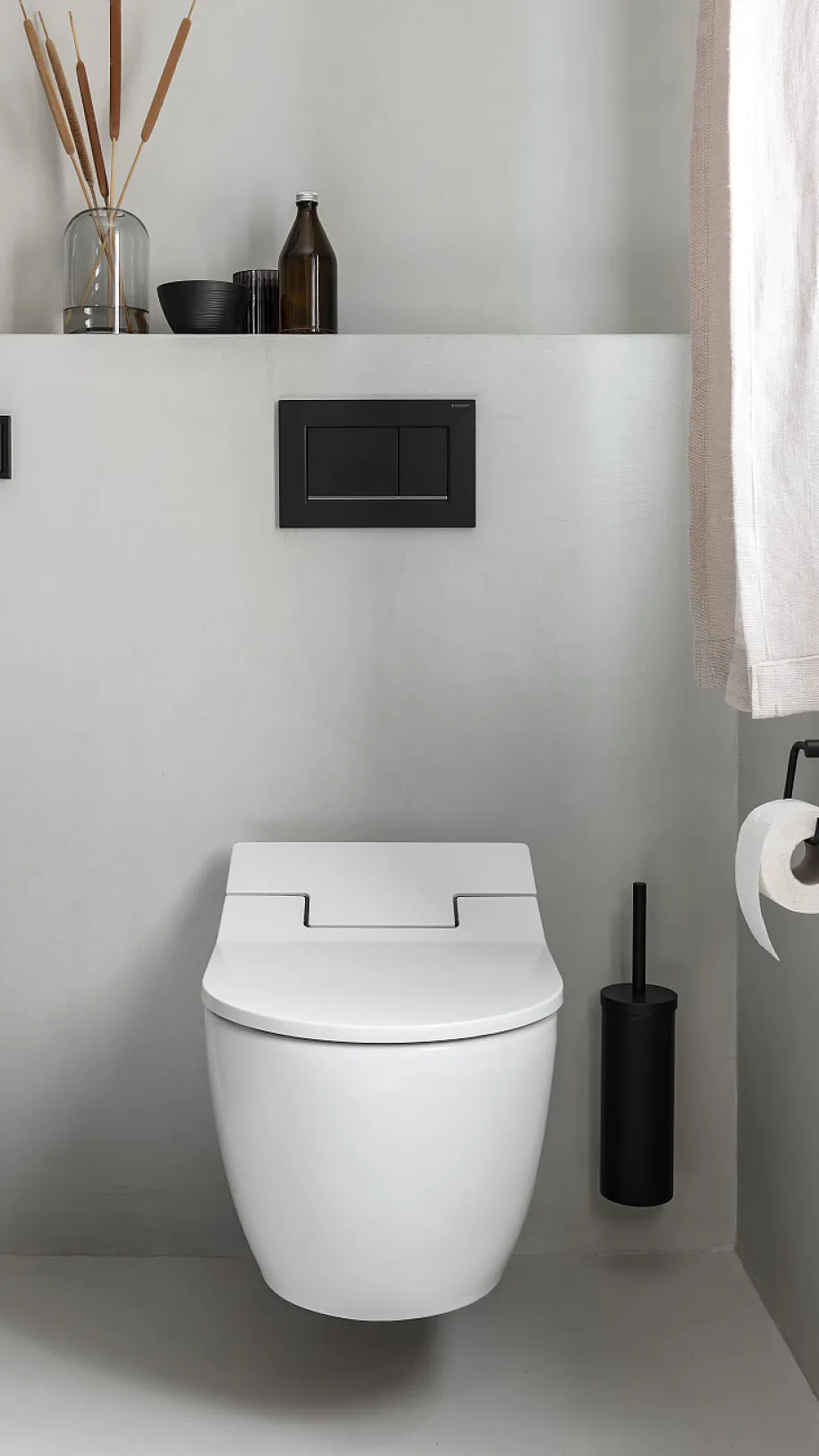 Weißes WC mit dunkler Bedienplatte vor fugenloser Wand in Betonoptik.