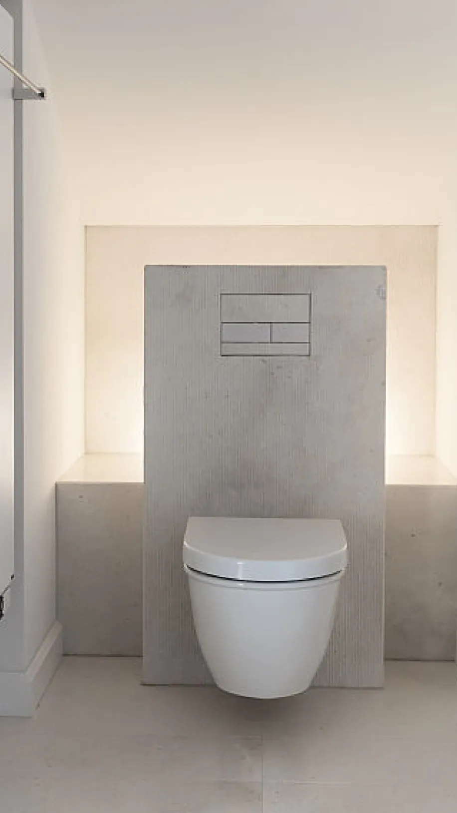 Die Toilette ist wandhängend und in einer Nische mit beigen Wänden und hellen Bodenfliesen installiert. Eine minimalistische Spülplatte ist in die Rückwand eingelassen.