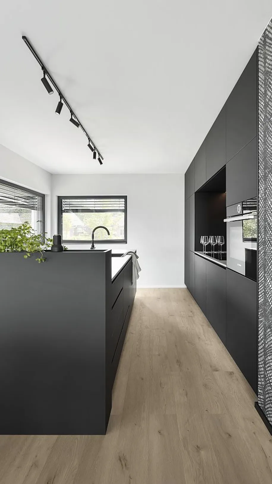 Küche in minimalistischem Design mit schwarzer Einrichtung, hellem Holzboden und Spotbeleuchtung an der Decke. Einbaugeräte und Dekorationen dezent platziert.