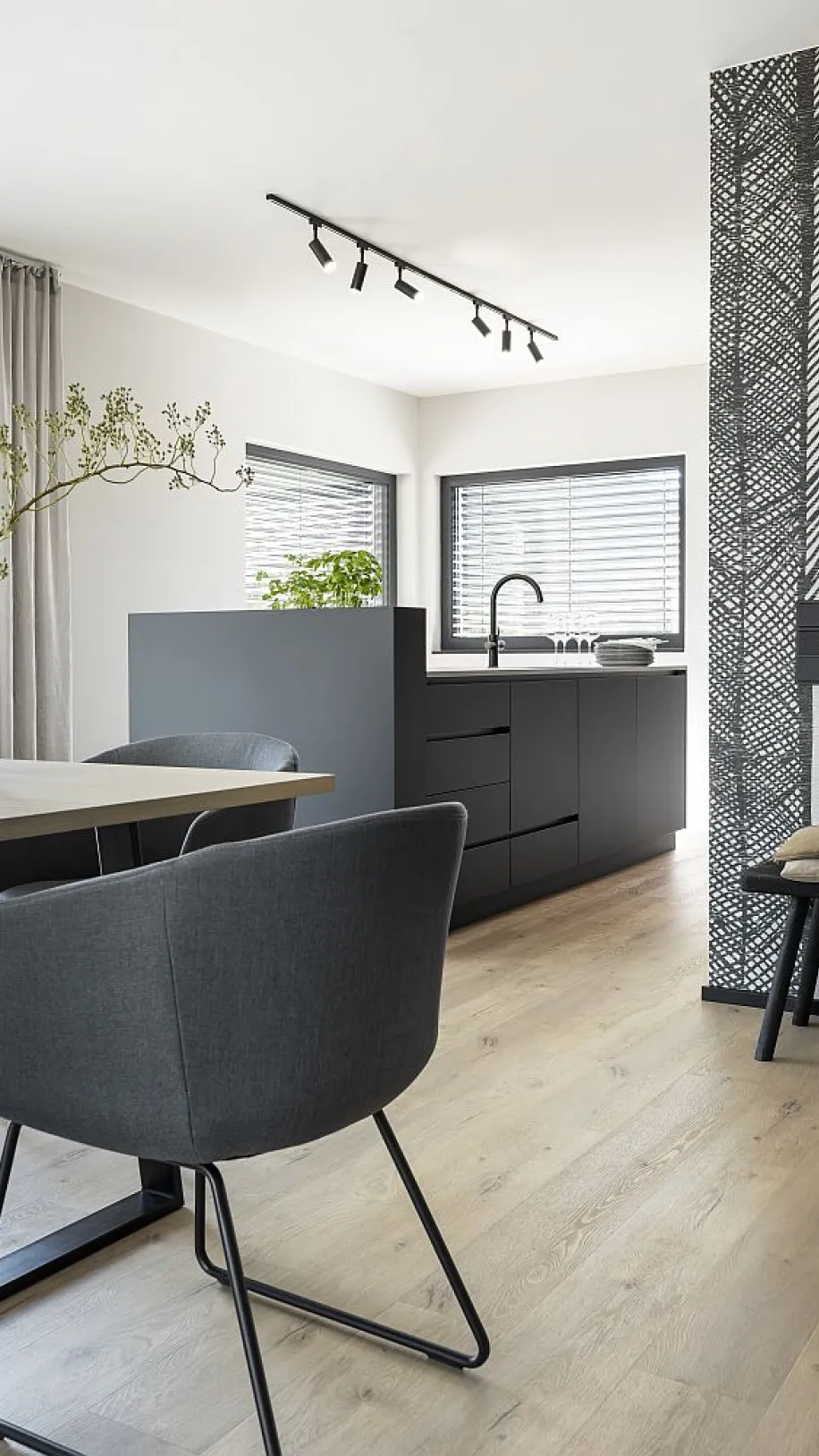 Essbereich mit grauem Stuhl und hellem Holztisch neben einer modernen Küche in dunklen Tönen.