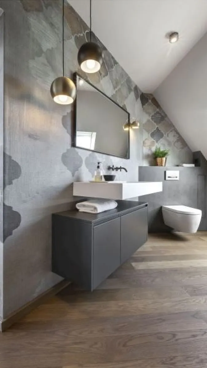 Modernes Badezimmer mit gemusterter Akzentwand, weißem Aufsatzwaschbecken, schwarzem Unterschrank und rechteckigem Spiegel. Rechts befindet sich eine schwebende Toilette, links zwei Hängelampen.