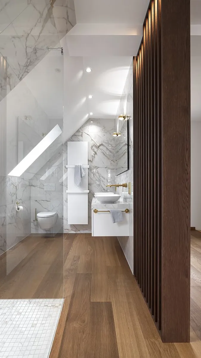 Ein modernes Badezimmer mit einer schrägen Decke, das durch einen Holzlamellen-Raumtrenner strukturiert wird.