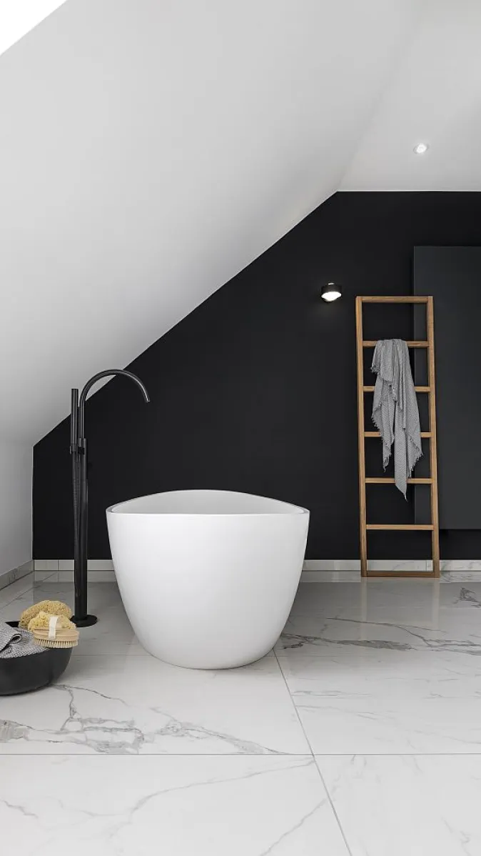 Badezimmer mit einer freistehenden, runden Badewanne vor einer schwarzen Wand und einem Handtuchhalter in Form einer Holzleiter.
