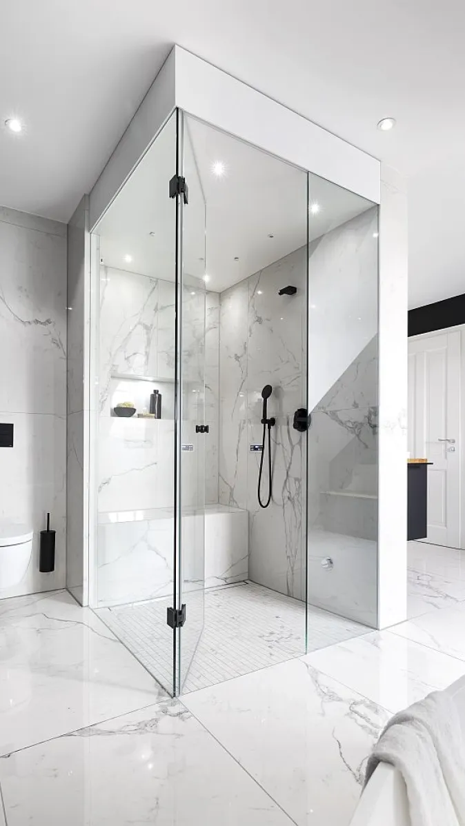 Badezimmer mit einer Glas-Dampfdusche, ausgestattet mit Marmorwänden und einer Sitzbank.