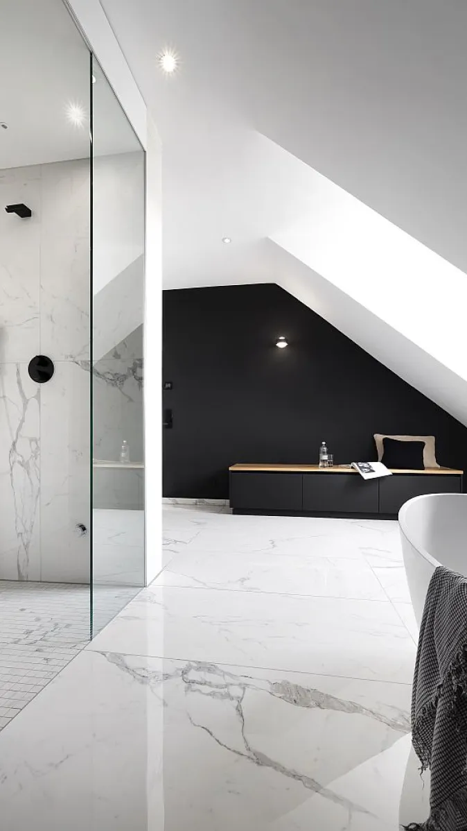 Helles Badezimmer mit Marmorfliesen, einer Glasdusche, einem dunklen Sideboard und einer freistehenden Badewanne in einer Dachschräge.