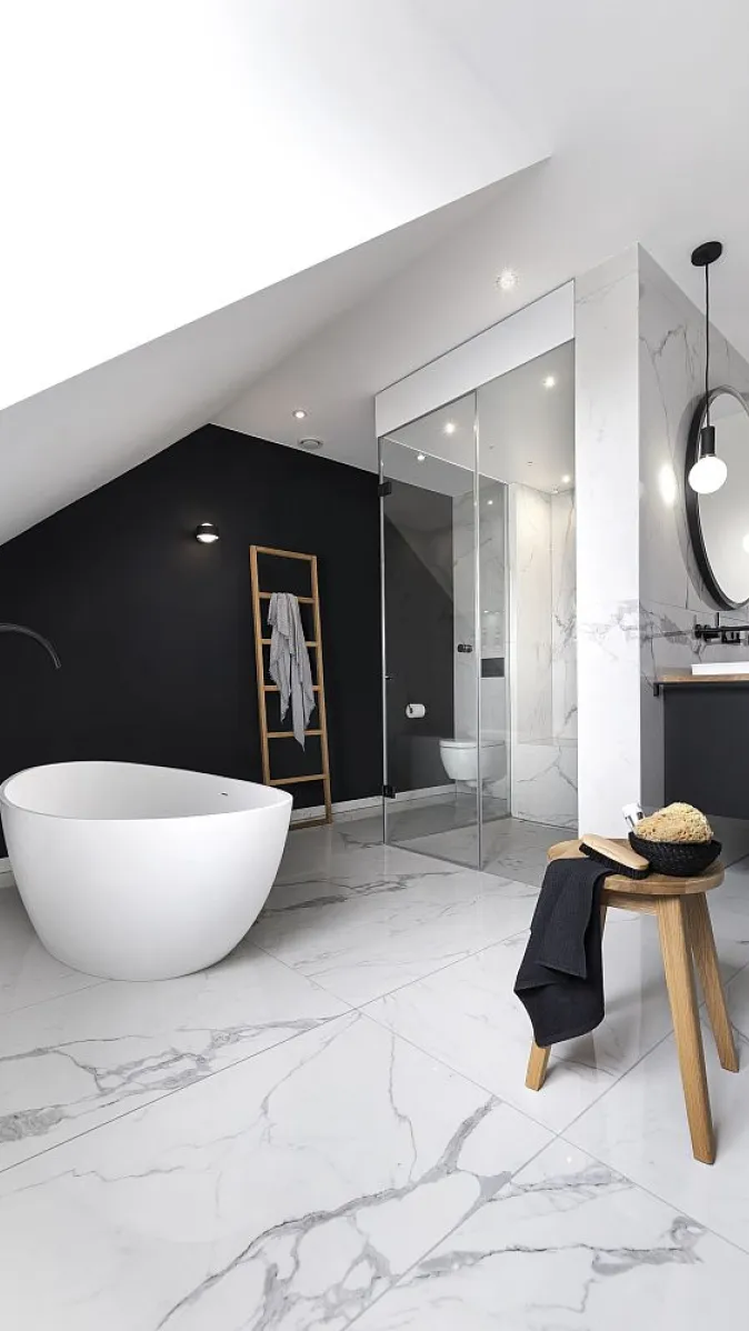 Wellnessbad mit einer freistehenden Badewanne, schwarzen Akzenten und einer Glas-Dampfdusche unter einer Dachschräge.