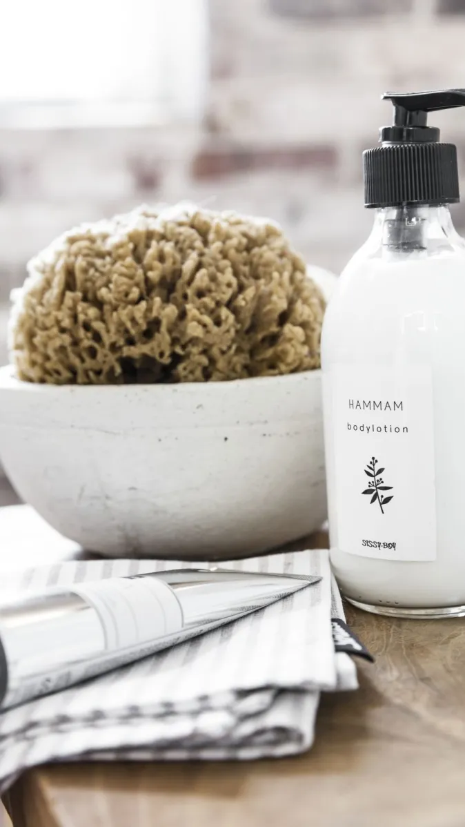 Badaccessoires auf einem Holztisch mit Schwamm, Hammam-Bodylotion und einer Metalltube.