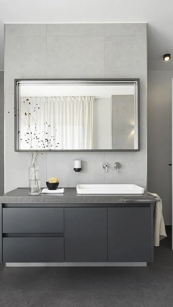 Minimalistisches Badezimmer mit grauen Wänden, Waschtisch und rechteckigem Spiegel. Einfache Dekorationselemente verleihen dem Raum Eleganz.