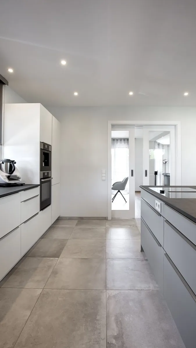 Helle Küche mit weißer Küchenzeile, Bodenfliesen und Schiebetür.