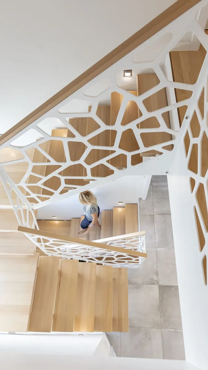 Von oben fotografierte Holztreppe mit einer markanten weißen Brüstung, die aus unregelmäßigen geometrischen Formen besteht.