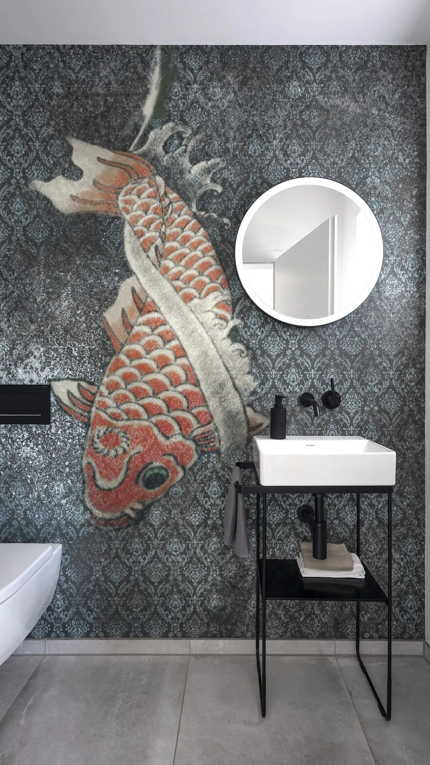 Gäste-WC mit einer auffälligen Akzentwand, die einen großen, roten Koi-Fisch auf einem dunklen, gemusterten Hintergrund zeigt. Ein minimalistisches, weißes Waschbecken auf einem schwarzen Metallgestell steht rechts, darüber hängt ein runder Spiegel.
