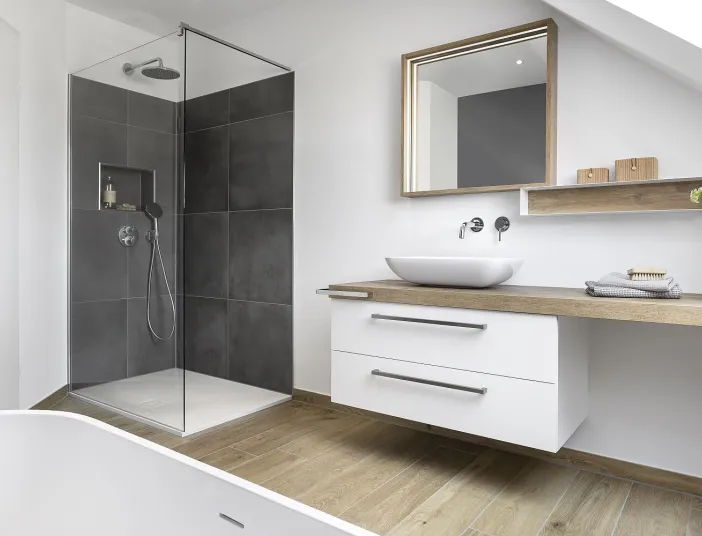 Dachbadezimmer mit dunkler Glasdusche und schwebendem Waschtisch mit Holzdetails.