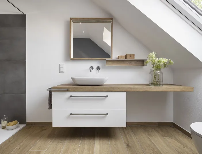 Dachbadezimmer mit einem Waschtisch aus Holz und einem weißen Aufsatzwaschbecken, das direkt unter der Dachschräge platziert ist.