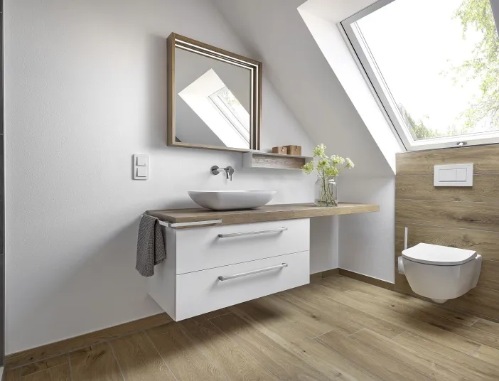 Dachbadezimmer mit schwebendem Waschtisch in Holzoptik und wandmontierter Toilette vor einer Wandverkleidung aus hellem Holz.