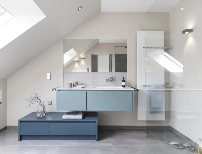 Badezimmer unter einer Dachschräge mit einem hängenden, hellblauen Waschtisch und einem großen Spiegel darüber.