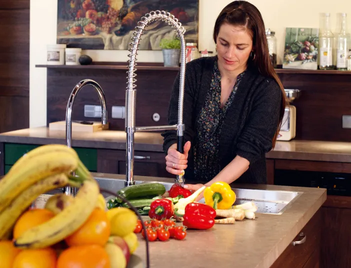 Frau in einer modernen Küche reinigt mit einem großen ausziehbaren Wasserhahn Obst und Gemüse.