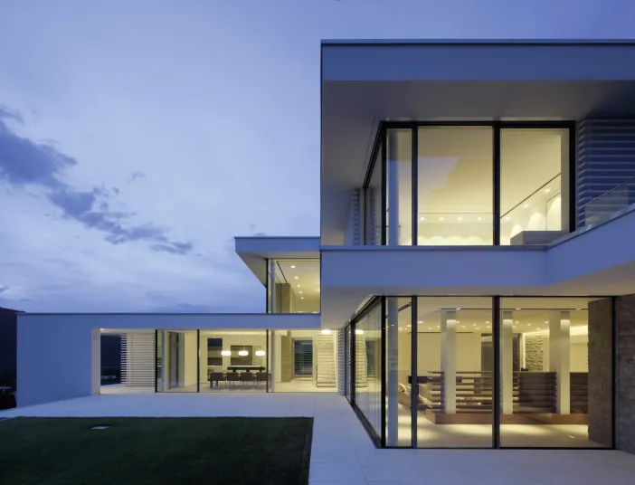 Ein zeitgenössisches Wohnhaus mit großen Glasfronten und kubischem Design bei Dämmerung.